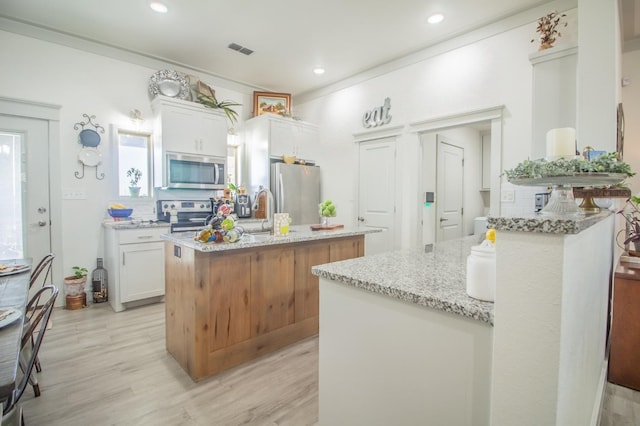 kitchen with light hardwood / wood-style flooring, stainless steel appliances, light stone counters, white cabinets, and a kitchen island