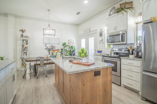 kitchen featuring sink, appliances with stainless steel finishes, pendant lighting, a kitchen island with sink, and white cabinets