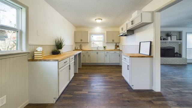 kitchen featuring butcher block counters, white cabinetry, dark hardwood / wood-style floors, a fireplace, and a textured ceiling