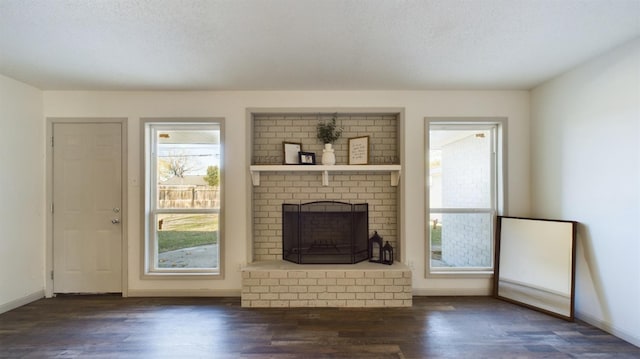 unfurnished living room featuring dark wood-type flooring, a brick fireplace, and a textured ceiling