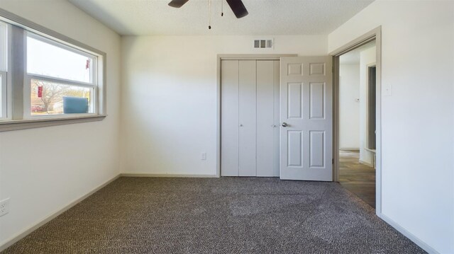 unfurnished bedroom with ceiling fan, dark carpet, and a closet