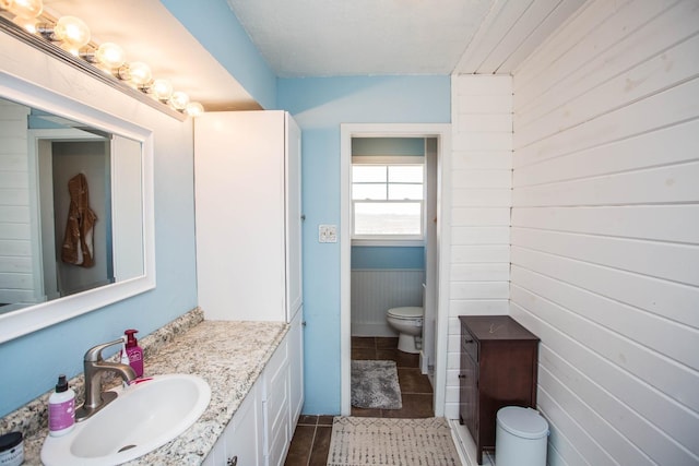 bathroom featuring vanity, toilet, tile patterned flooring, and wood walls