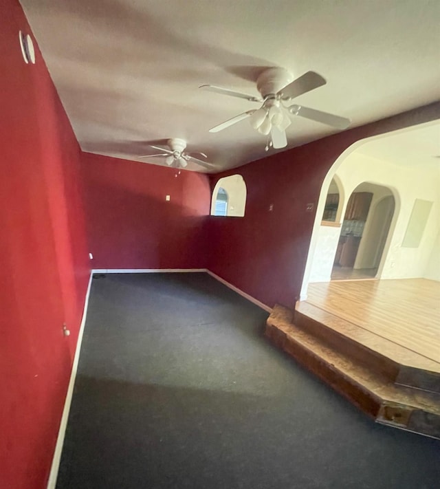 carpeted empty room with arched walkways, a ceiling fan, and baseboards