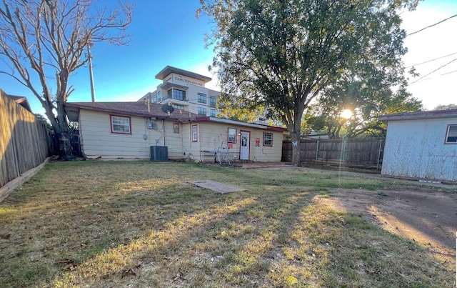 rear view of property featuring central air condition unit, a fenced backyard, and a lawn