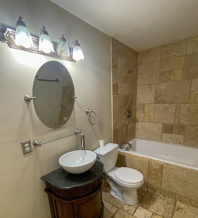 full bathroom with stone tile flooring, tiled shower / bath combo, vanity, and toilet