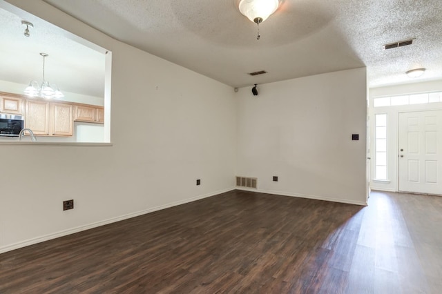 unfurnished living room with dark hardwood / wood-style flooring, sink, a textured ceiling, and an inviting chandelier