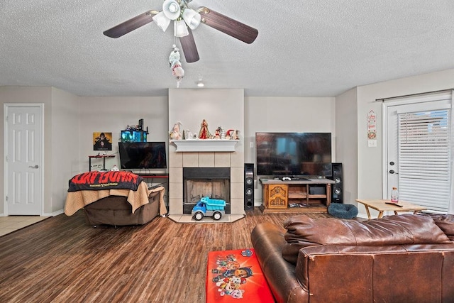 living room featuring hardwood / wood-style flooring, ceiling fan, a fireplace, and a textured ceiling