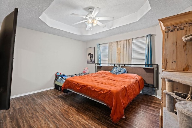 bedroom with a textured ceiling, dark wood-type flooring, a raised ceiling, and ceiling fan