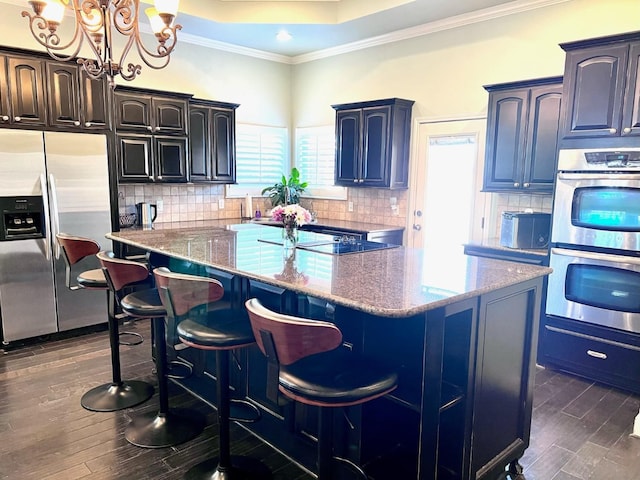 kitchen with hanging light fixtures, stainless steel appliances, ornamental molding, a kitchen island, and dark hardwood / wood-style flooring