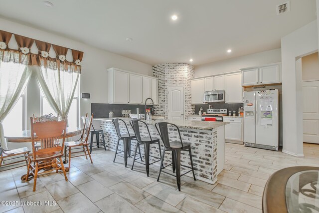 14320 Ave U, Lubbock, TX 79423 - kitchen with stainless steel appliances, tasteful backsplash, white cabinetry, a kitchen breakfast bar, and light stone counters