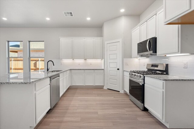 kitchen with sink, light hardwood / wood-style flooring, appliances with stainless steel finishes, light stone countertops, and white cabinets