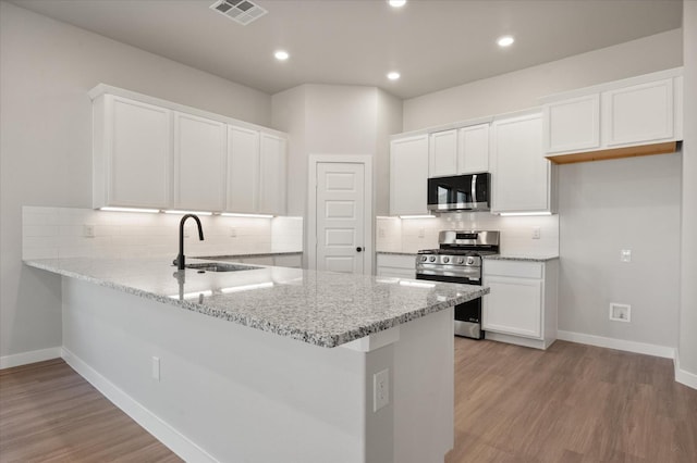 kitchen with sink, light wood-type flooring, kitchen peninsula, stainless steel appliances, and white cabinets