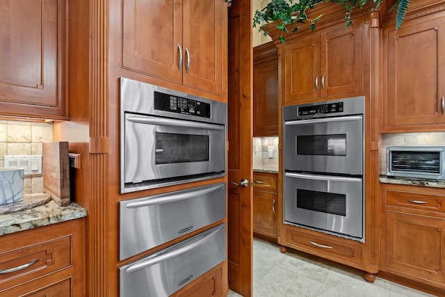 kitchen with light stone counters, decorative backsplash, stainless steel double oven, and light tile patterned flooring