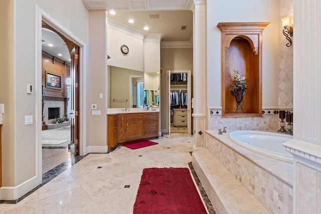 bathroom with a large fireplace, ornamental molding, vanity, and tiled tub