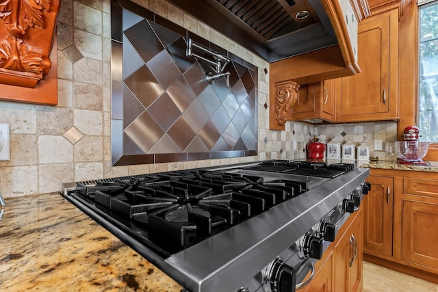 interior space featuring tasteful backsplash, wall chimney exhaust hood, range, and light stone countertops