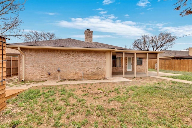 back of property featuring a chimney, a fenced backyard, a yard, brick siding, and a patio