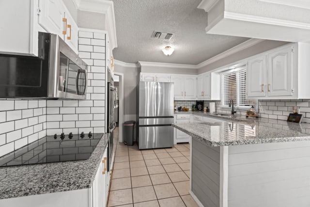 kitchen with light tile patterned flooring, white cabinetry, crown molding, kitchen peninsula, and stainless steel appliances