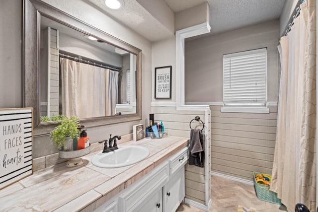 bathroom with parquet flooring, vanity, a textured ceiling, and wood walls