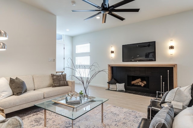 living room with ceiling fan, wood-type flooring, and a tiled fireplace