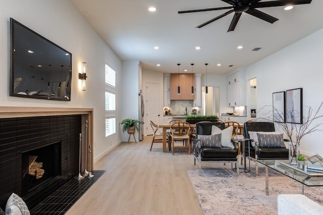 living room with a tiled fireplace, light hardwood / wood-style flooring, and ceiling fan