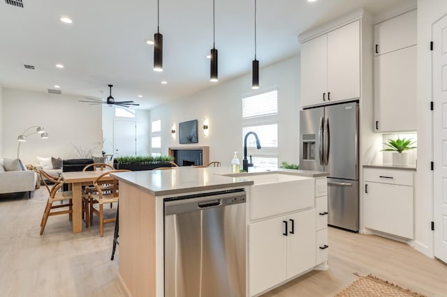 kitchen with white cabinetry, appliances with stainless steel finishes, pendant lighting, and a center island with sink