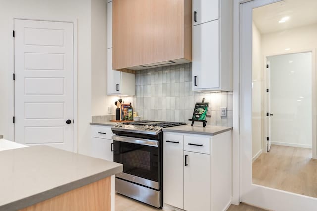 kitchen featuring tasteful backsplash, white cabinetry, stainless steel range with gas stovetop, and light brown cabinetry