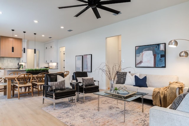 living room featuring ceiling fan, sink, and light wood-type flooring