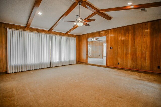 empty room with wooden walls, lofted ceiling with beams, ceiling fan, light carpet, and a textured ceiling