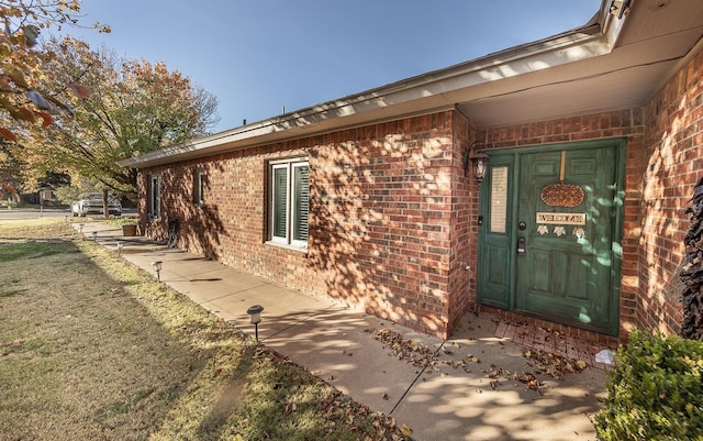 doorway to property featuring a lawn and brick siding