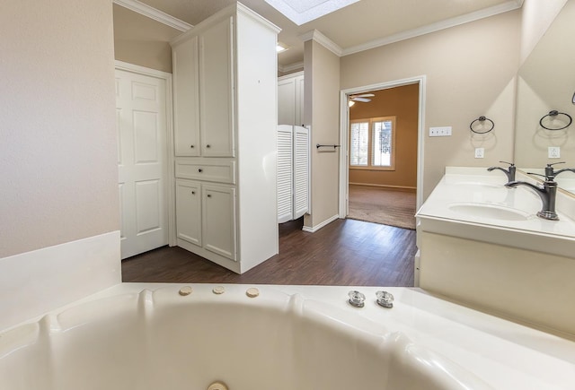 bathroom with ceiling fan, wood finished floors, a garden tub, crown molding, and a sink