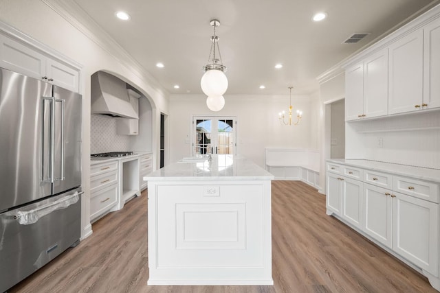 kitchen featuring white cabinetry, appliances with stainless steel finishes, wall chimney range hood, and decorative light fixtures