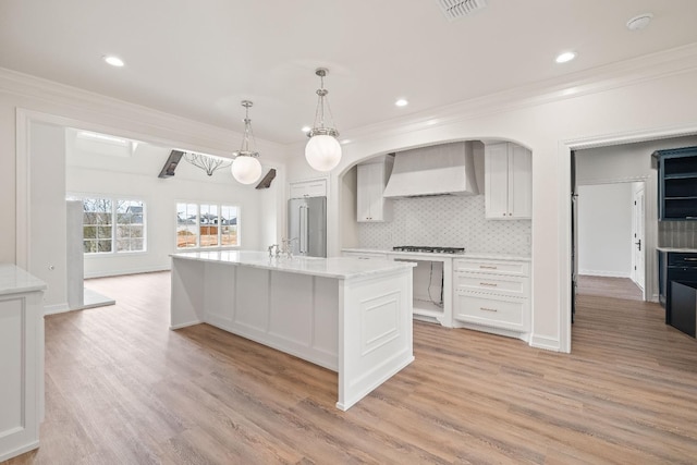 kitchen featuring white cabinets, hanging light fixtures, stainless steel appliances, crown molding, and wall chimney range hood