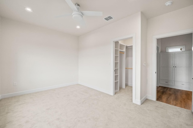 unfurnished bedroom featuring a spacious closet, light colored carpet, a closet, and ceiling fan