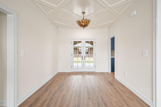 spare room with coffered ceiling, hardwood / wood-style floors, an inviting chandelier, and french doors