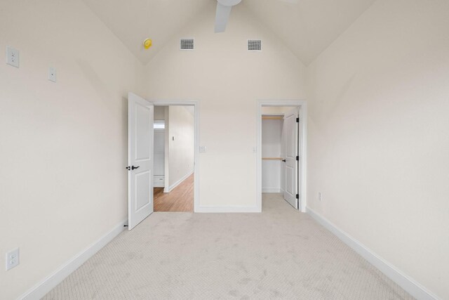 unfurnished bedroom with a walk in closet, light colored carpet, high vaulted ceiling, and a closet