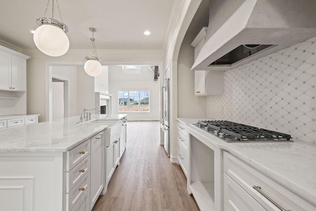 kitchen with pendant lighting, stainless steel appliances, custom range hood, white cabinets, and a center island with sink