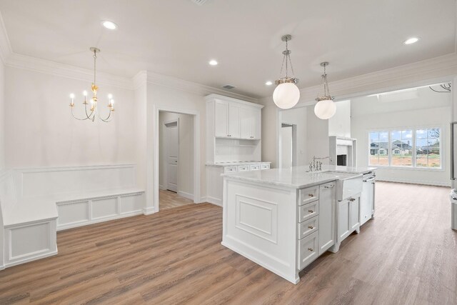 kitchen with a center island with sink, ornamental molding, dishwasher, pendant lighting, and white cabinets