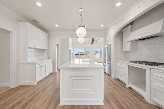 kitchen featuring white cabinetry, hanging light fixtures, a kitchen island with sink, stainless steel appliances, and wall chimney exhaust hood