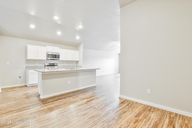 2012 Kenwood Ave, Lubbock, TX 79407 - kitchen featuring stainless steel appliances, white cabinetry, a center island with sink, light wood-type flooring, and light stone counters