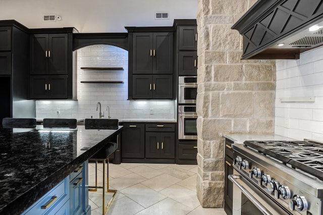 kitchen featuring light tile patterned floors, premium range hood, dark stone countertops, backsplash, and stainless steel appliances