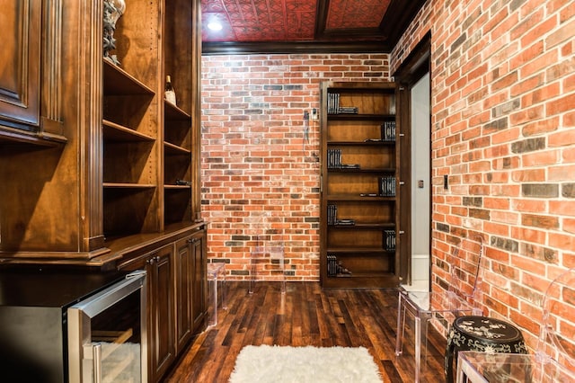 wine room with dark wood-type flooring, brick wall, crown molding, and beverage cooler