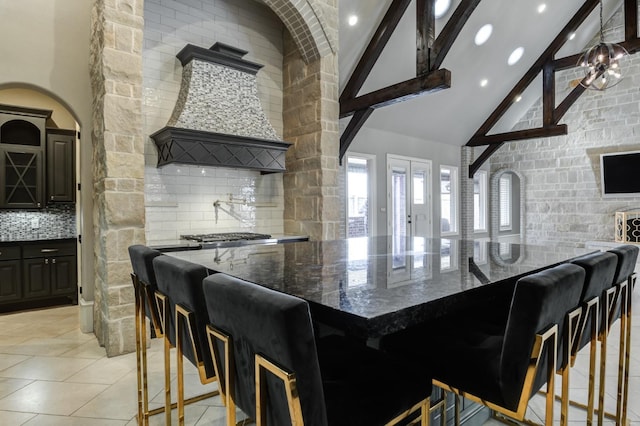 kitchen with high vaulted ceiling, a breakfast bar area, decorative backsplash, dark stone counters, and a spacious island