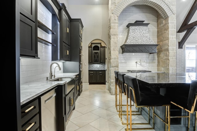 kitchen featuring light stone counters, decorative backsplash, stainless steel dishwasher, and a kitchen bar