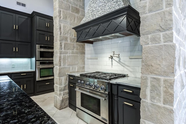 kitchen with light stone counters, light tile patterned floors, appliances with stainless steel finishes, custom range hood, and decorative backsplash