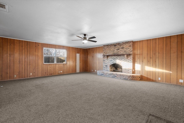 unfurnished living room with a fireplace, wood walls, ceiling fan, and carpet flooring