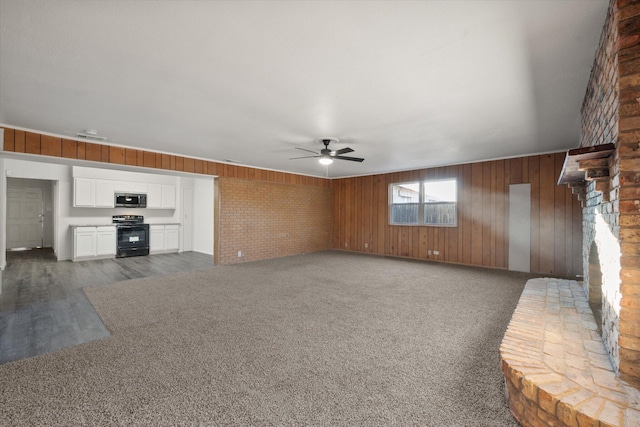 unfurnished living room featuring dark carpet, wooden walls, and ceiling fan