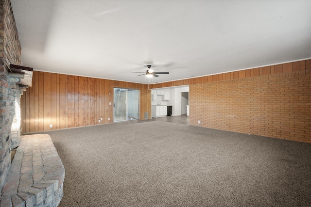 unfurnished living room featuring ceiling fan, brick wall, carpet flooring, and wood walls