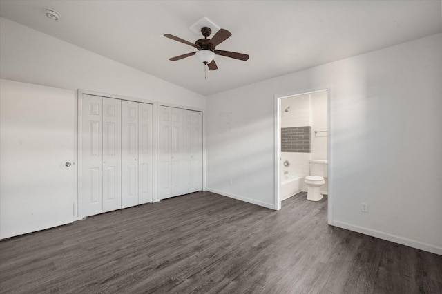 unfurnished bedroom with vaulted ceiling, connected bathroom, dark hardwood / wood-style floors, and two closets