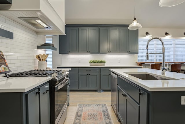 kitchen with sink, appliances with stainless steel finishes, light hardwood / wood-style floors, custom range hood, and a center island with sink