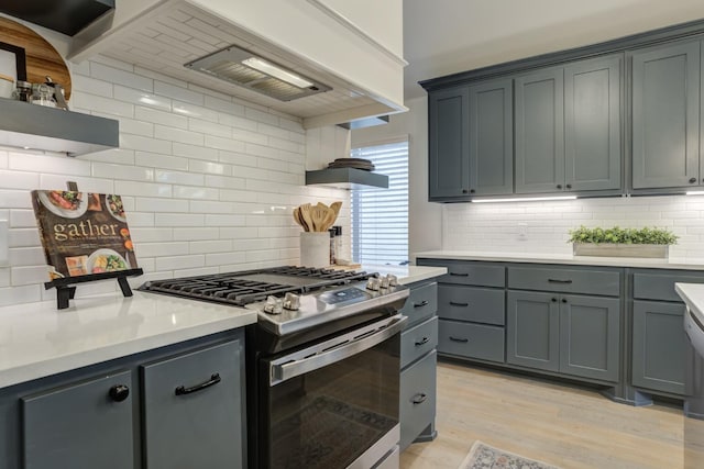 kitchen featuring gray cabinetry, decorative backsplash, custom exhaust hood, light hardwood / wood-style floors, and stainless steel gas range oven